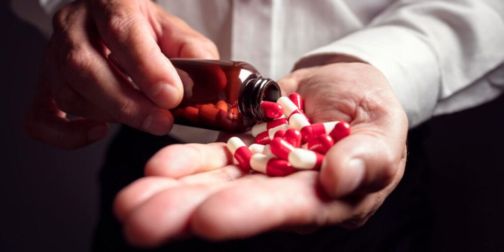 A person pours red and white capsules into their hand, illustrating the 3-day Rule For Methadone and its dosage.